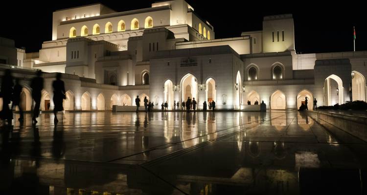 Casa de ópera de mármol iluminada reflejándose en la plaza pulida bajo el cielo nocturno.