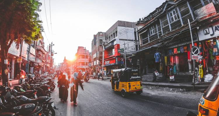 Rue indienne animée au coucher du soleil avec des auto-rickshaws, des boutiques et des habitants marchant dans la lumière dorée.