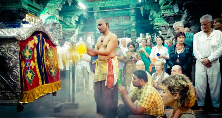Un prêtre effectue un rituel à l'intérieur d'un temple sud-indien orné, entouré de touristes attentifs au milieu de la fumée d'encens.