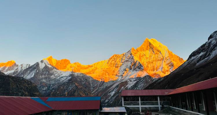 Golden sunrise light bathes jagged Himalayan peaks behind colorful teahouse rooftops in the Annapurna range.