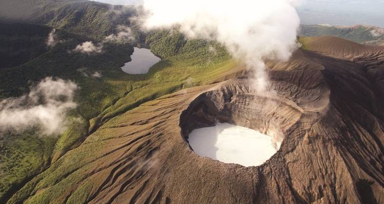 Luchtfoto van een grote krater met opstijgende stoom, omringd door groene vegetatie.