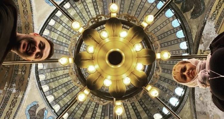 People looking up at a decorative chandelier inside a historical building.