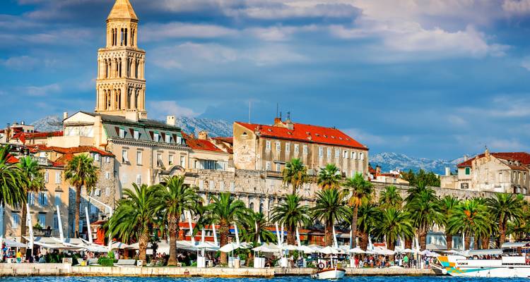 Historische Uferpromenade mit Palmen und einer Kathedrale.