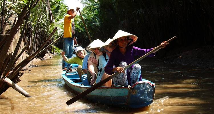 Menschen paddeln mit einem traditionellen Boot durch einen schmalen Kanal.