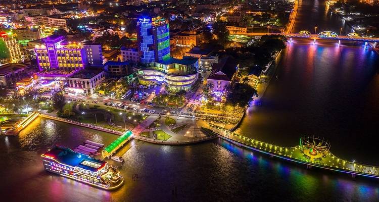 Nachtansicht einer lebendigen Stadt mit beleuchteten Gebäuden und einem Fluss.