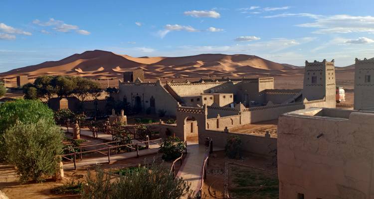 Traditionelle marokkanische Gebäude mit Wüstendünen im Hintergrund.
