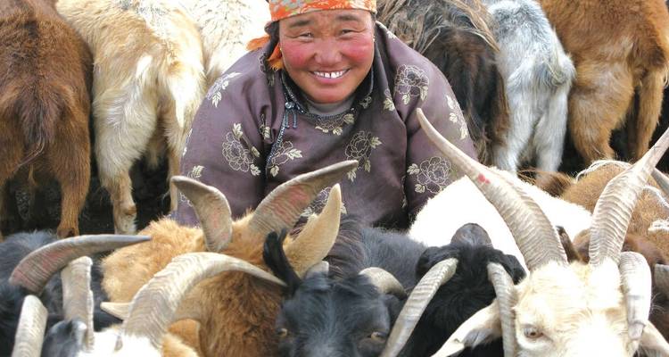 Una mujer sonriendo rodeada de un rebaño de cabras.