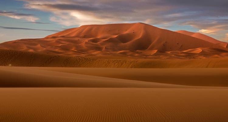 Wüstendünen bei Sonnenuntergang mit einem orangefarbenen Himmel.