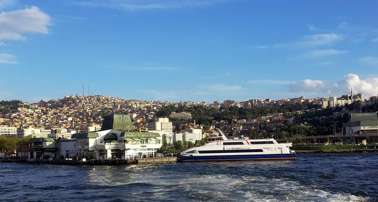 Veerboot op zee met een stadsgezicht van laagbouw gebouwen op de achtergrond.