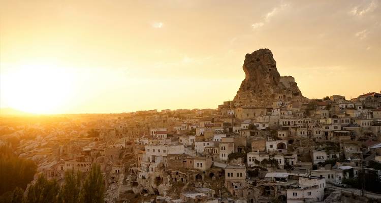 Zonsondergang over een rotsachtig landschap met historische gebouwen in Cappadocië.