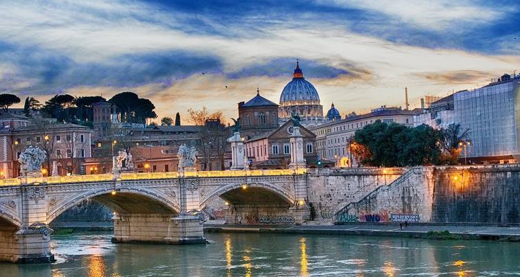 Bridge over a river with historic buildings and a dome at twilight.
