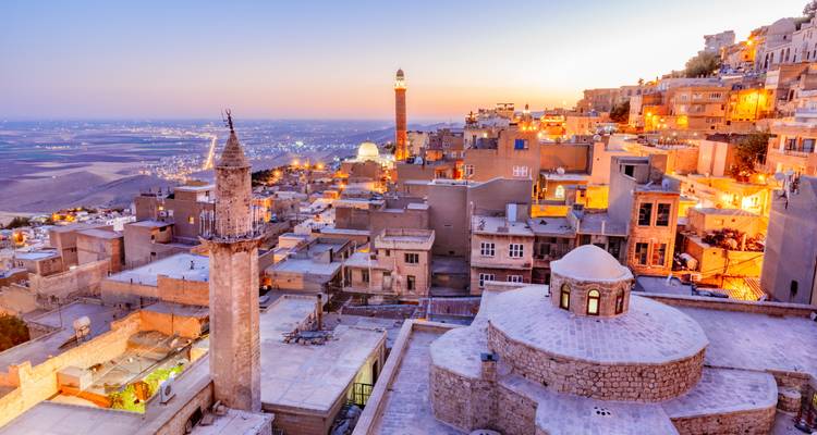 Paysage urbain de Mardin avec bâtiments illuminés et tours historiques au coucher du soleil.