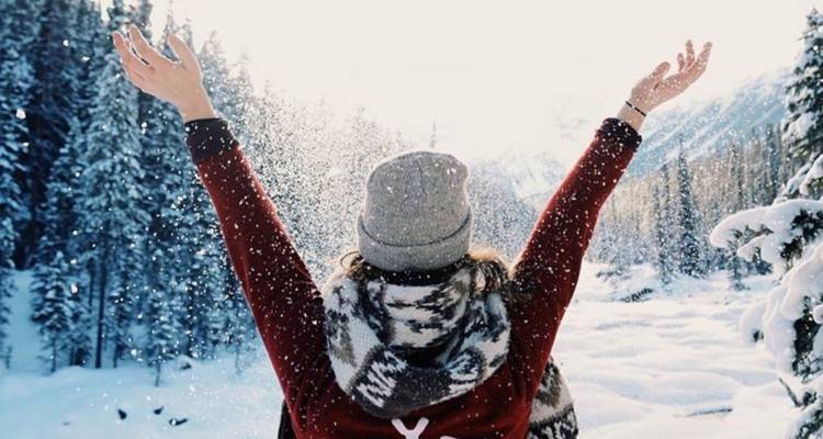 Person, die den Winter genießt, indem sie Schnee in die Luft wirft.