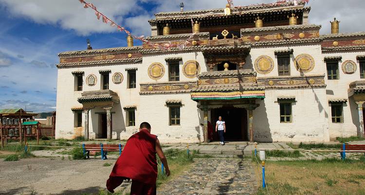 Monk in red robe enters a historic Buddhist monastery adorned with golden symbols on the façade.