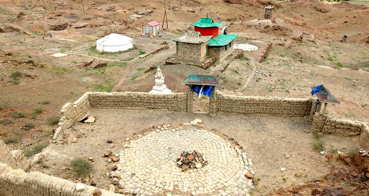 Stone walls, a small temple with green roofs and surrounding dry, rocky terrain in the Mongolian steppe.
