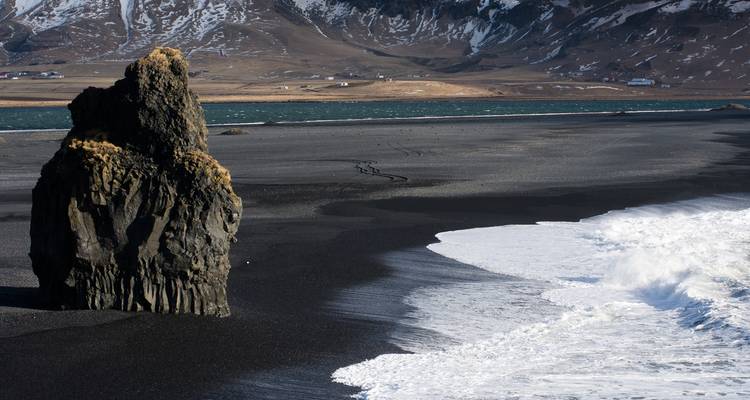 Rotsformatie op een zwart zandstrand.