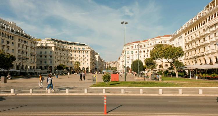 Broad Aristotelous Square in Thessaloniki filled with walkers and cafes framed by neoclassical buildings.