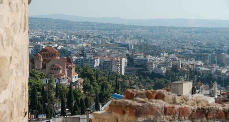 Distant view over Thessaloniki’s sprawling cityscape with a prominent brick church amid green cypress trees.