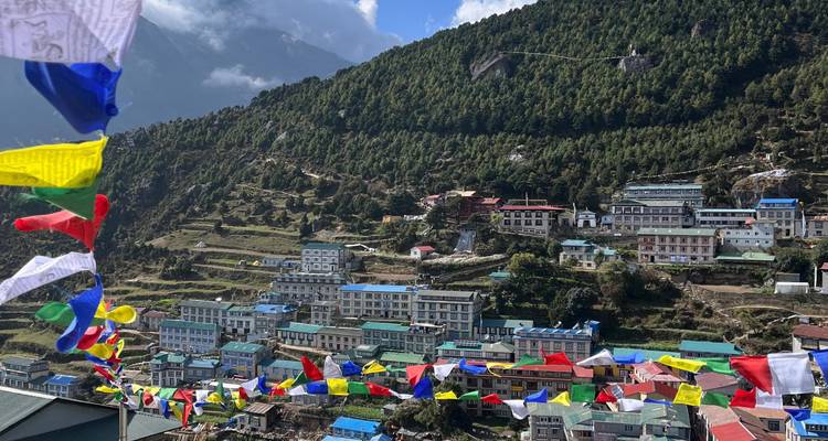 Kleurrijke gebedsvlaggen met een dorp tegen een bergachtige achtergrond.