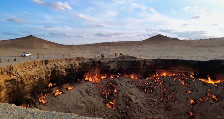 Cratère de gaz Darvaza en feu au milieu d'un paysage désertique austère avec des visiteurs sur le bord.