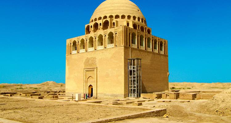 Large ancient brick mausoleum with a domed roof standing alone in a desert landscape under a vivid blue sky.