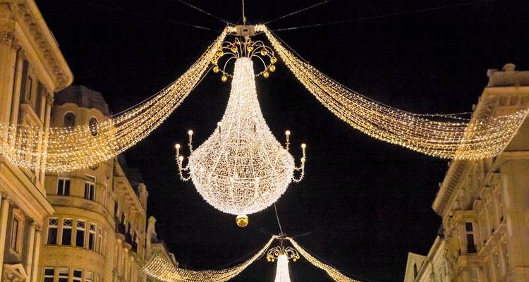 Opulentas arañas de cristal y guirnaldas de luces cuelgan sobre una histórica calle comercial europea por la noche