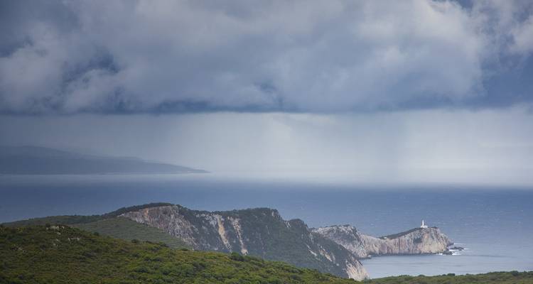 Stürmische Wolken über einer Küstenlandschaft mit einem Leuchtturm.