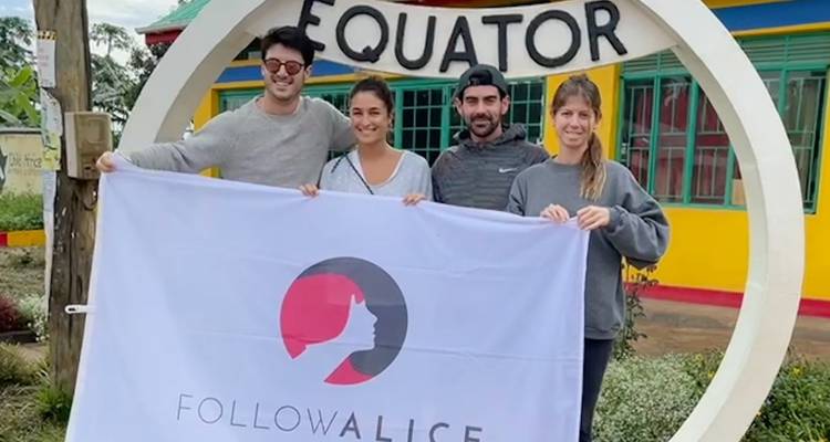 Group of people posing with a banner in front of an equator monument.