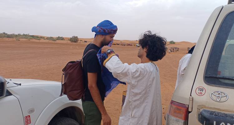 Zwei Personen, die in einer Wüstenumgebung in der Nähe von Fahrzeugen interagieren.