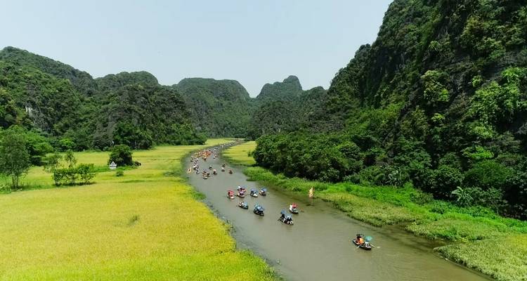 River with small boats navigating through it, surrounded by green mountains and fields.