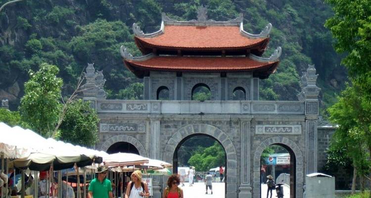 Een traditionele stenen poort met toeristen die eromheen lopen, weelderig groen op de achtergrond.