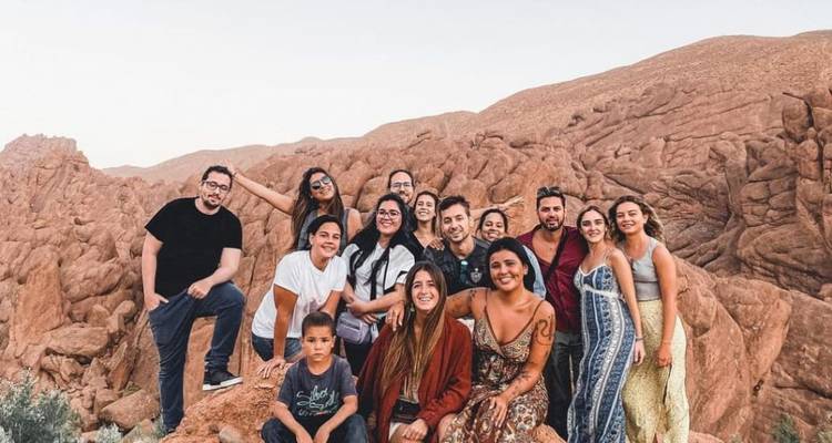Grote groep lachende reizigers die poseren tussen roodachtige rotsformaties in een ruig canyonlandschap.
