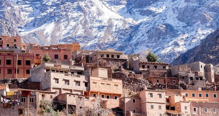 Traditionele Berberdorphuizen gestapeld op een helling met besneeuwde Atlasbergen die errond oprijzen.