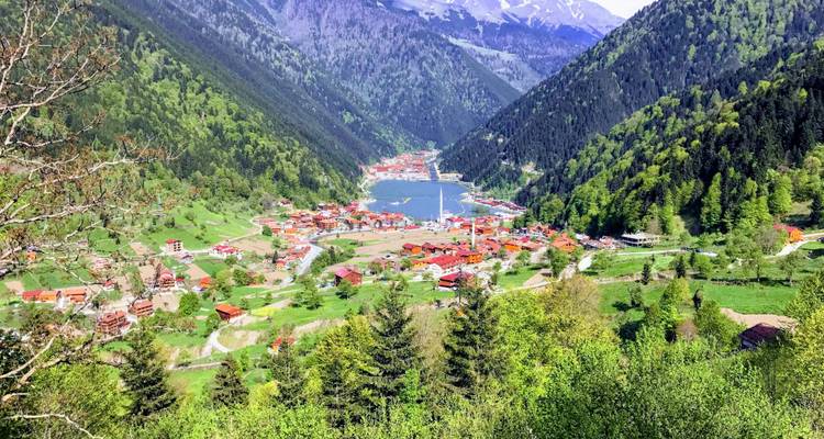 Vista aérea de un valle con un lago y un pueblo rodeados de montañas.