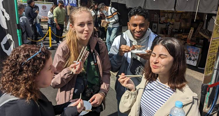 Groupe savourant de la nourriture de rue avec des expressions souriantes, fond de marché animé.