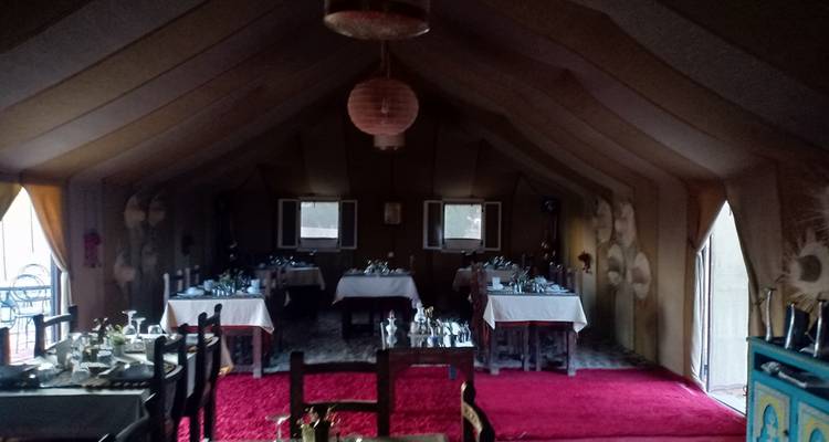 Dentro de una carpa comedor débilmente iluminada con mesas y sillas preparadas para una comida.