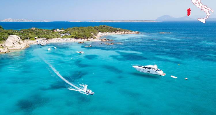 Aerial view of turquoise Sardinian bay dotted with yachts and a speedboat leaving a white wake