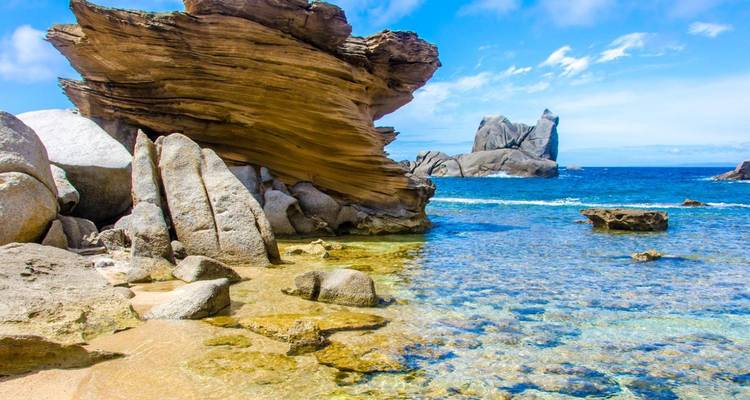 Clear blue sea lapping against dramatic wind-carved granite rocks on a sunny Sardinian coast