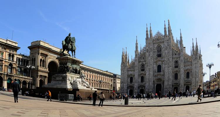 Het Piazza del Duomo in Milaan met de grootse gotische kathedraal en ruiterstandbeeld onder een blauwe hemel.
