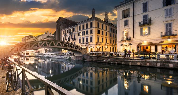 Zonsondergang gloeit over Milaan's Navigli kanalendistrict, met bruggen en kleurrijke gebouwen die reflecteren in het kalme water.