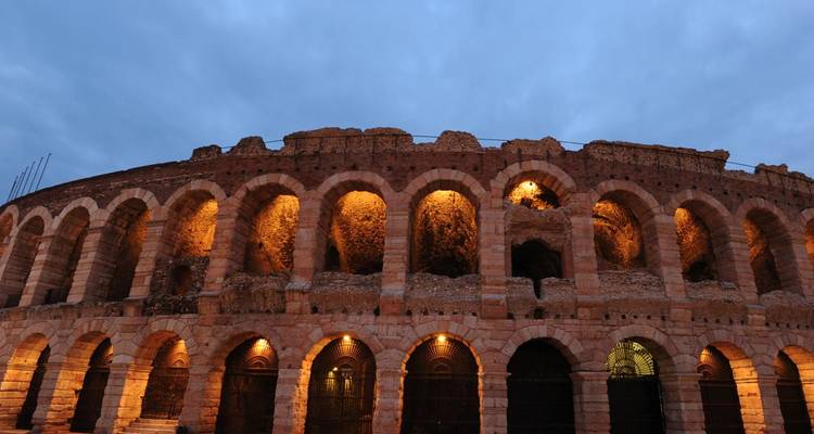 Anfiteatro romano en Verona iluminado por luces cálidas contra un cielo azul crepuscular.