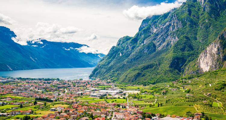 Vista panorámica desde las alturas de un gran lago alpino bordeado por empinadas montañas verdes que descienden hacia un pueblo vibrante.