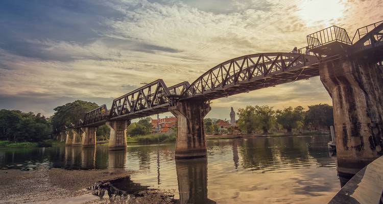 Un puente histórico de acero se extiende sobre un río tranquilo al atardecer con reflejos en el agua.