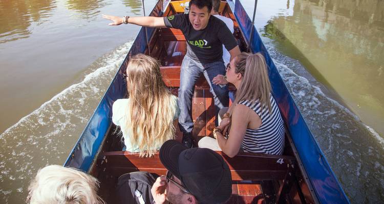 El guía señala lugares de interés a los viajeros mientras deslizan por un canal turbio en una barca de cola larga.
