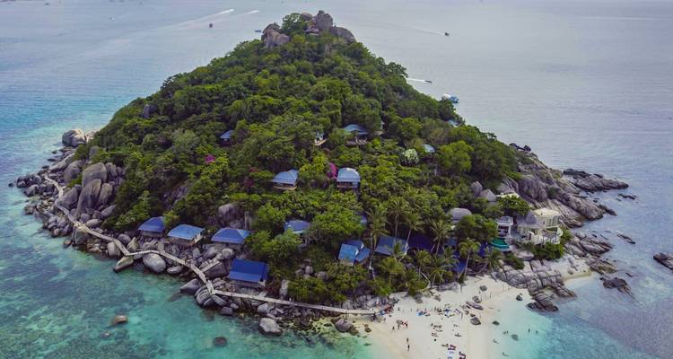 Luftaufnahme einer grünen Insel, umgeben von Korallenriffen und Booten
