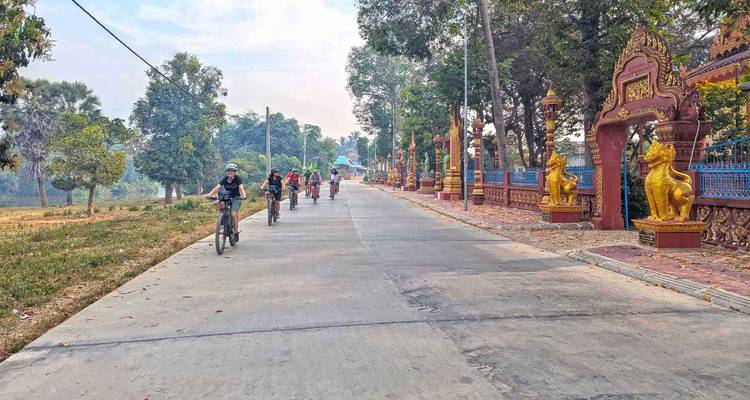 Los ciclistas andan en bicicleta por un camino rural tranquilo de Camboya bordeado de portadas de templo ornamentadas y estatuas.