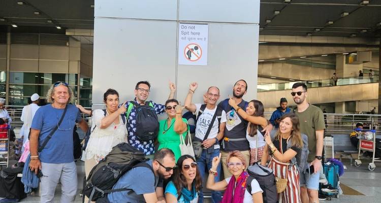 Gruppe posiert am Flughafen unter einem Schild mit Spuckverbot.