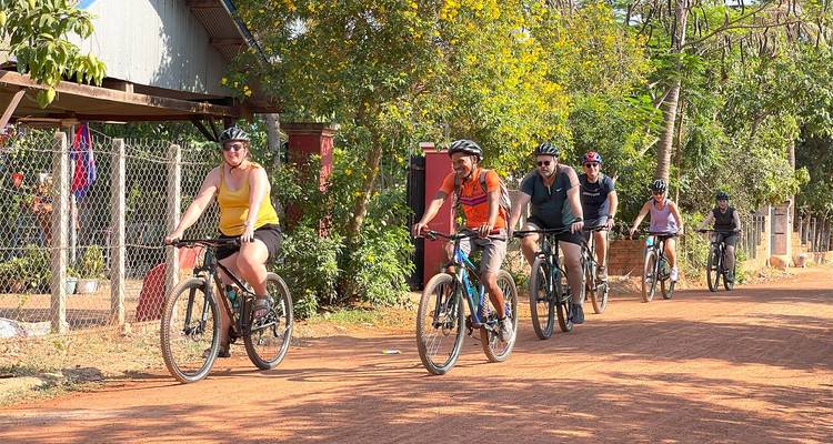 Grupo de ciclistas internacionales pedaleando por una calle de pueblo iluminada por el sol
