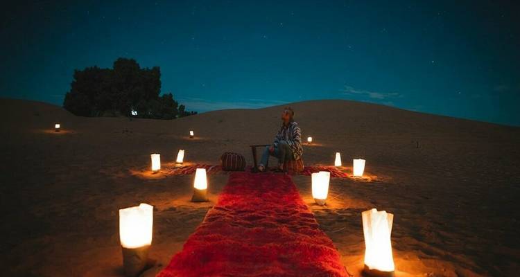 Individu in een woestijnomgeving, omringd door verlichte lantaarns onder de nachtelijke hemel.
