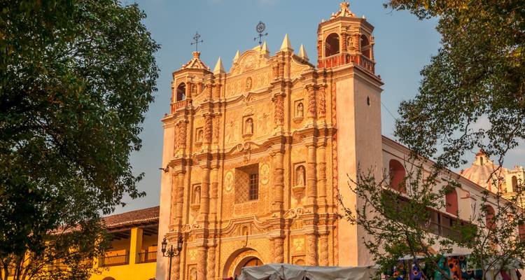 Prächtige koloniale Kirchenfassade, die in warmem Nachmittagslicht badet und von belaubten Bäumen in Chiapas umrahmt wird.